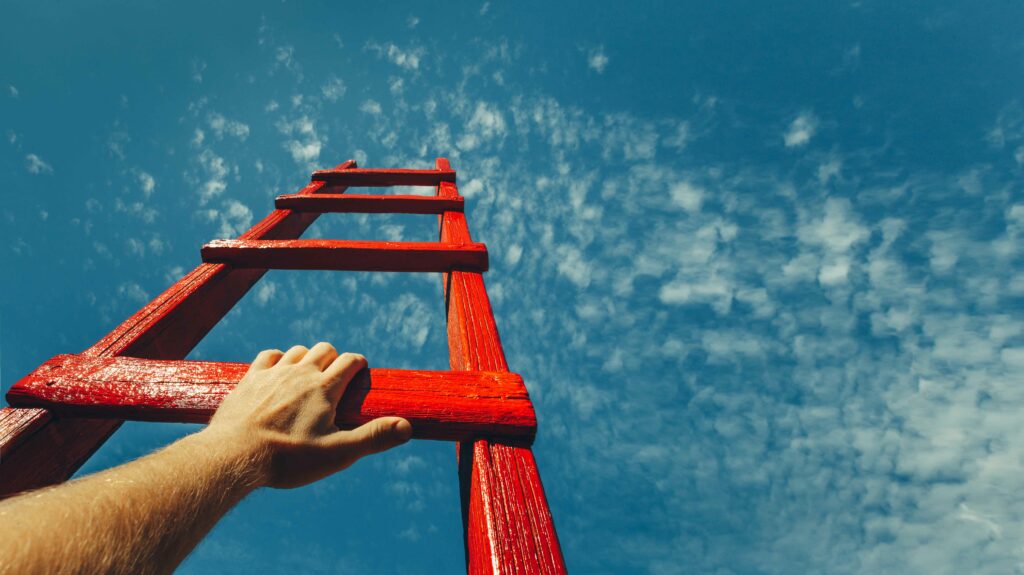 Development-Attainment-Motivation-Career-Growth-Concept.-Mans-Hand-Reaching-For-Red-Ladder-Leading-To-A-Blue-Sky