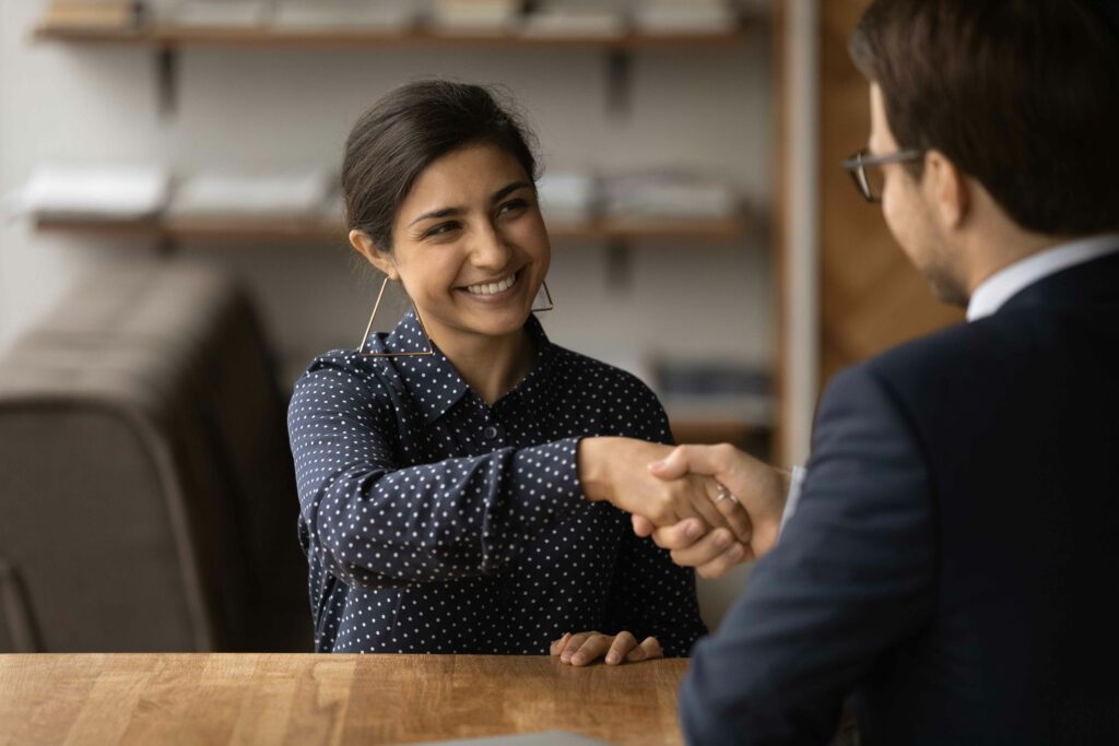 Salutations, on vous engage. Une jeune Indienne heureuse et brillante chercheuse d'emploi serra la main d'un directeur des ressources humaines masculin accepté sur un lieu vacant. Divers partenaires commerciaux s'entendent sur un accord de clôture