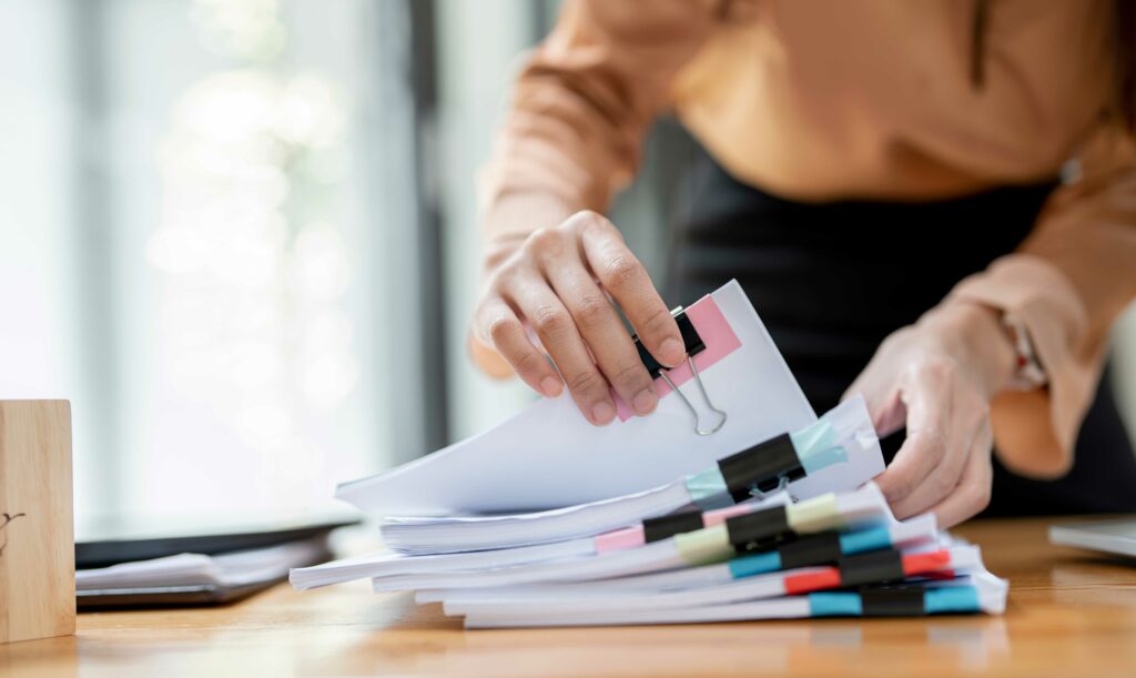 Des mains de femme d'affaires travaillant dans des piles de fichiers papier pour rechercher et vérifier des documents inachevés réussissent sur des dossiers papiers au bureau de travail occupé